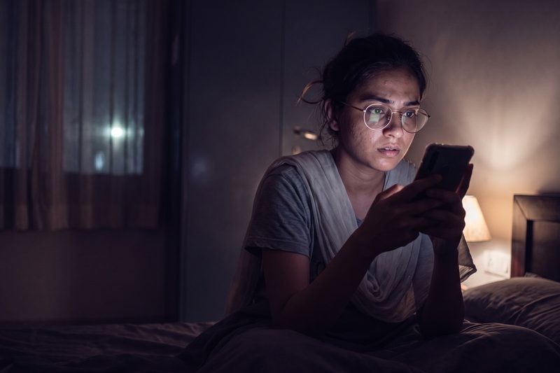 A young woman sitting up in bed late at night, taking over a conversation on her phone